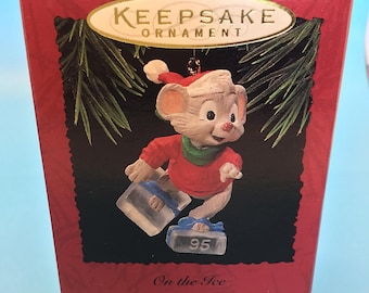 May include: A red Keepsake Ornament box with a cartoon mouse figure wearing a red sweater, green scarf, and blue ice skates. The ornament is from 1995 and is titled "On the Ice."