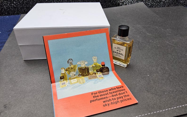 May include: A perfume bottle with a black cap sits next to a pop-up card featuring various perfume bottles. The card has text that reads, "For those who love the most luxurious perfumes&mdash;but don't wish to pay the sky-high prices."