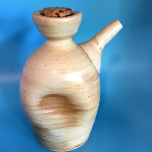 May include: A handmade ceramic pitcher with a cork stopper. The pitcher is beige with brown swirl patterns and a spout. The design is a unique, handcrafted piece for serving beverages.