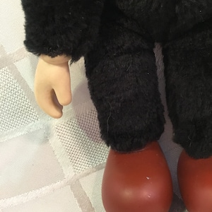 Puede incluir: Primer plano de las piernas y el brazo de una mu&ntilde;eca. La mu&ntilde;eca tiene pantalones negros difusos y una chaqueta negra difusa. Los pies de la mu&ntilde;eca son de color marr&oacute;n rojizo y el brazo es de tono claro.