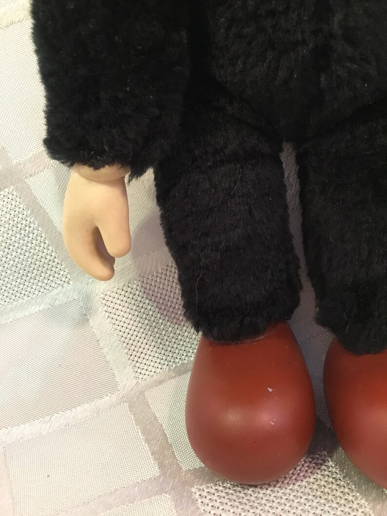 Puede incluir: Primer plano de las piernas y el brazo de una mu&ntilde;eca. La mu&ntilde;eca tiene pantalones negros difusos y una chaqueta negra difusa. Los pies de la mu&ntilde;eca son de color marr&oacute;n rojizo y el brazo es de tono claro.