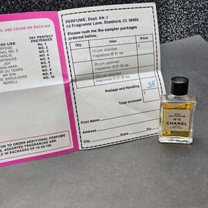 May include: A small bottle of Chanel No. 5 Eau de Parfum sits next to a pink and white perfume identification chart and an order form. The perfume bottle has a black cap and a gold label. The order form lists sampler packages.