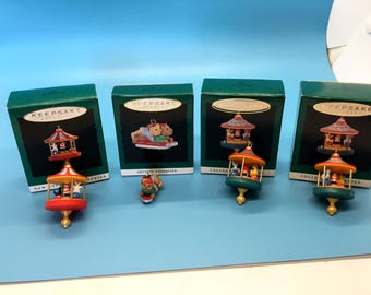 May include: Four Hallmark Keepsake Christmas ornaments. The ornaments are carousel-themed, with red, yellow, and green colours. Each ornament is displayed with its original green box. The boxes have gold lettering and a gold oval.