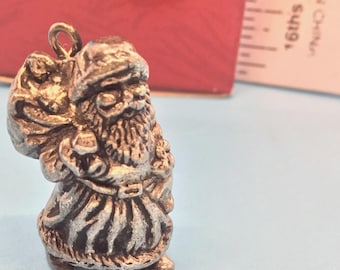 May include: A small, silver-coloured Santa Claus figurine with a sack over his shoulder. The figurine has a detailed beard, hat, and coat. The Santa Claus figurine is a Christmas-themed item.