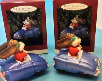 May include: Two Hallmark Keepsake ornaments showing a dog in a blue convertible. The dog is wearing a red top and green goggles. The car has the words "Super Sports Brother". The ornaments are in their original boxes.