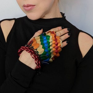 May include: A rainbow-colored metal hand covering with a chain bracelet. The hand covering is made of overlapping scales and is worn on the left hand.