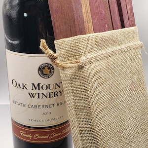 May include: A set of four wine barrel stave coasters in a burlap bag. The coasters are made of wood and have a natural finish. The bag has a drawstring closure and is made of burlap.