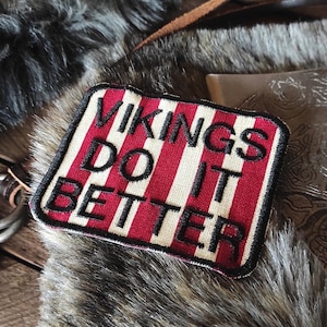 May include: A red and white striped patch with black embroidered text that reads "Vikings Do It Better".