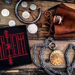 May include: A black patch with red embroidery that reads "DANHEIM". The patch is surrounded by silver coins and a leather pouch with a wooden bead. A silver chain with a brass pendant featuring a rune symbol is also pictured.
