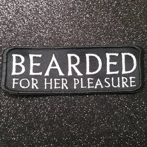 Puede incluir: Un parche rectangular negro con texto bordado en blanco que dice "BEARDED FOR HER PLEASURE". El parche está sobre un fondo negro brillante.
