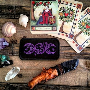 Peut inclure: Un patch noir avec un symbole de triple lune violet, entouré d'étoiles, sur une surface en bois avec des cartes de tarot, des cristaux et un couteau en pierre.