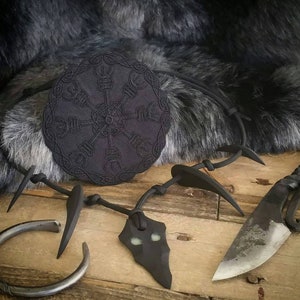 May include: Black necklace with a pendant shaped like a jagged stone with a green glow. The necklace is made of black cord and has several black spikes. A black circular pendant with a symbol is also included.