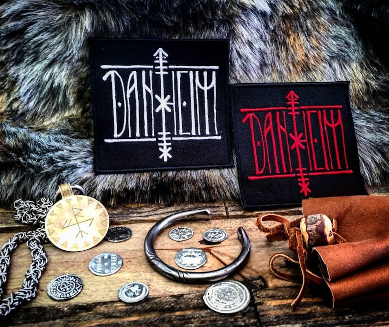 May include: Two black fabric patches with the word "DANHEIM" embroidered in white and red thread. The patches are on a furry surface with a gold chain and a metal bracelet with coins.