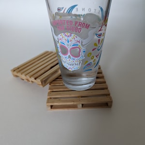 May include: A clear glass with a colorful skull design and the text "Imported from San Diego" is sitting on two wooden coasters.