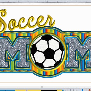 Può includere: Un "MOM" argentato scintillante con un pallone da calcio al centro. La parola "Soccer" è sopra le lettere in un font corsivo dorato. Le lettere sono circondate da un bordo a strisce blu, giallo e arcobaleno.