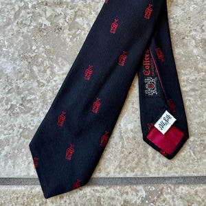 Könnte beinhalten: Schwarze Seidenkrawatte mit rotem Muster eines Kaffeewagens. Die Krawatte hat ein rotes Futter und ein Etikett mit der Aufschrift "All Silk". Ein klassisches Accessoire.