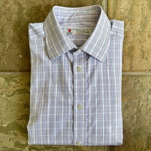 May include: A folded, button-down shirt with a white and blue plaid pattern. The shirt has a classic collar and is made of a lightweight fabric. The label reads "TURNBULL & ASSER" and "Exclusive".