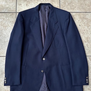 May include: A navy blue blazer with a classic design. The blazer features a two-button closure, two front pockets, and three buttons on each cuff. The interior lining is a muted gray color.