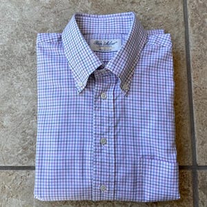 May include: A folded button-down shirt with a grid pattern in light purple, white, and navy blue. The shirt has a button-down collar and a chest pocket. The brand name "Ben Silver" is visible on the collar.
