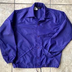 May include: A purple nylon jacket with a snap closure and a drawstring at the bottom.