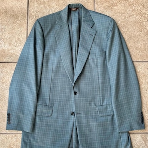 Peut inclure: Un blazer bleu clair avec un motif à carreaux bleu foncé subtil, un revers cranté, deux boutons sur le devant, deux poches à rabat et quatre boutons sur chaque poignet. Le vêtement est entièrement doublé avec un intérieur sombre et structuré.
