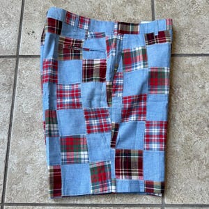 May include: Patchwork shorts in a light blue fabric with red, green, and brown plaid squares. The shorts have a button and zipper closure and pockets. The shorts are made of a lightweight material.