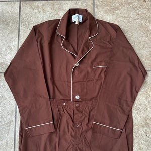 May include: Brown pajama set with white piping trim. The long-sleeved top has a button-down front and a notched collar. The pants have an elastic waistband. The set is made of a soft, comfortable material.