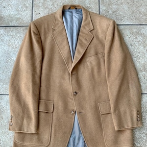 Op de afbeelding: Een bruin blazer met een lichtblauwe voering. De blazer heeft twee voorzakken, drie knopen op elke manchet en een sluiting met twee knopen. De jas is gemaakt van een zachte, getextureerde stof.