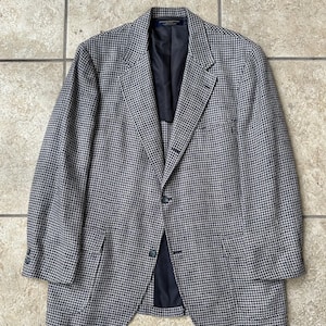 Puede incluir: Un blazer con estampado de pata de gallo en tonos azul marino y gris. La chaqueta presenta solapas con muescas, dos bolsillos delanteros y cierre de dos botones. El forro interior es azul marino liso.