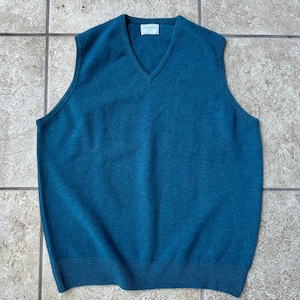 May include: Teal-colored V-neck sweater vest. The sleeveless garment has a ribbed hem and a small label near the neckline. The vest is made of a soft, knitted material. The vest is a classic style.
