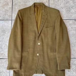 Pode incluir: Um blazer verde-oliva vintage com fecho de dois botões, lapelas entalhadas e dois bolsos frontais. O blazer tem um corte sob medida e um forro de cor clara. As mangas têm botões nos punhos. O blazer é feito de um tecido texturizado.