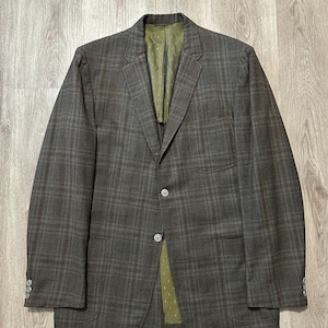May include: A brown and gray plaid blazer with a two-button closure and two front pockets. The blazer has a green lining and three buttons on each cuff. The fabric has a subtle texture.