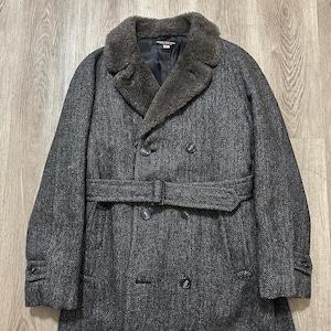 May include: A charcoal gray herringbone pattern overcoat with a faux fur collar and a belted waist. The double-breasted coat has button closures and buttoned cuffs. The coat is a classic style.
