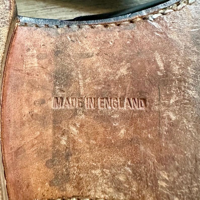 May include: Close-up of a worn leather shoe sole. The sole is brown with visible wear and stitching. The words "MADE IN ENGLAND" are embossed on the sole.