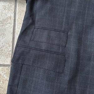 May include: A dark gray blazer with a single flap pocket on the left side.