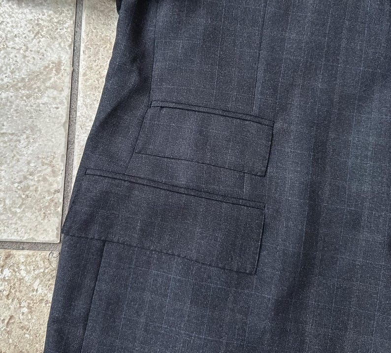 May include: A dark gray blazer with a single flap pocket on the left side.