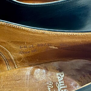 May include: Close-up of the interior of a leather shoe. The shoe's insole is a light brown colour, with visible text that reads "Last 89/D" and "Shoe No". The shoe's upper is a dark colour.