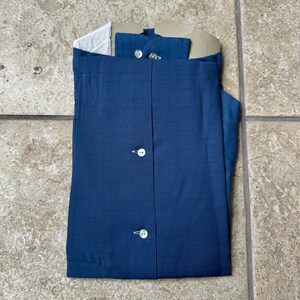 May include: A folded, navy blue button-down shirt with white buttons. The shirt is neatly packaged with a cardboard collar support and a white paper insert. The fabric has a subtle textured pattern.