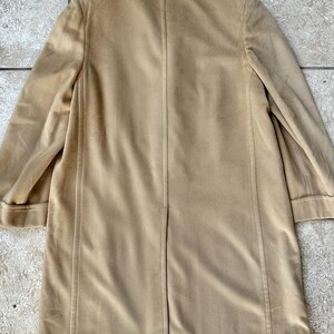 May include: A tan-colored coat with a classic design. The coat features a notched collar, long sleeves, and a button closure. The coat is made of a soft, suede-like material and has a tailored fit. The coat is a versatile piece for any wardrobe.