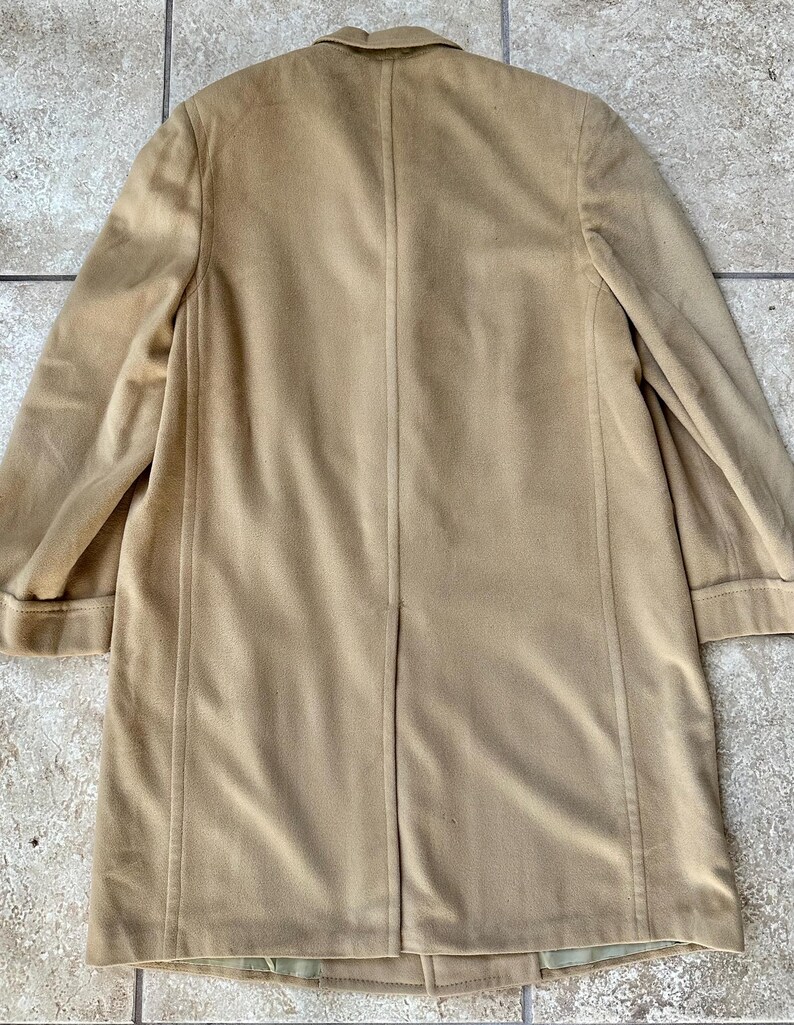 May include: A tan-colored coat with a classic design. The coat features a notched collar, long sleeves, and a button closure. The coat is made of a soft, suede-like material and has a tailored fit. The coat is a versatile piece for any wardrobe.
