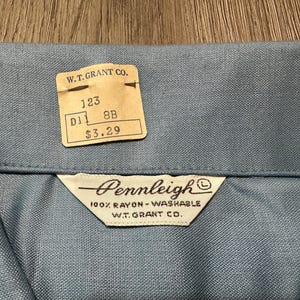 May include: A light blue shirt collar with a vintage W.T. Grant Co. paper price tag attached. The tag displays the text 123, D11, 8B, and $3.29. A white fabric label is sewn below the collar, reading Pennleigh, 100% Rayon-Washable, W.T. Grant Co.