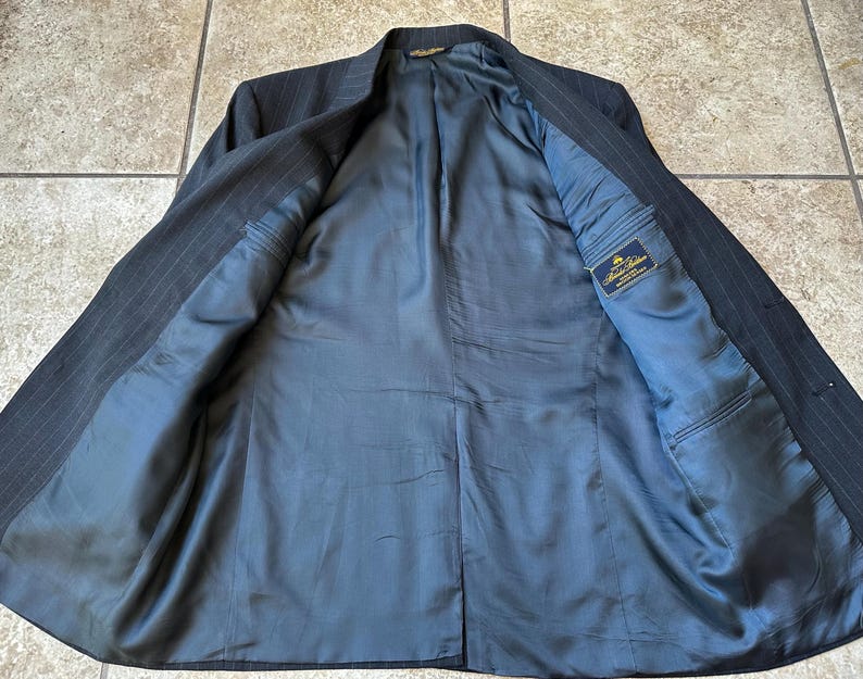 May include: A black pinstripe suit jacket with a blue lining. The lining has a small label that reads "Brooks Brothers".