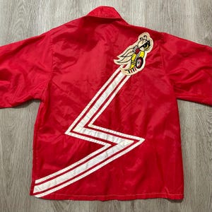 May include: Red vintage jacket with a white lightning bolt design and a cartoon bee patch. The jacket has a collared neckline and short sleeves. The bee patch is yellow, black, and white.