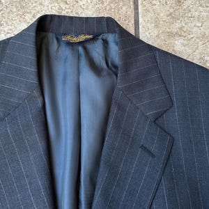 May include: A dark gray pinstripe suit jacket with a blue lining. The jacket has a single button closure and a notch lapel.