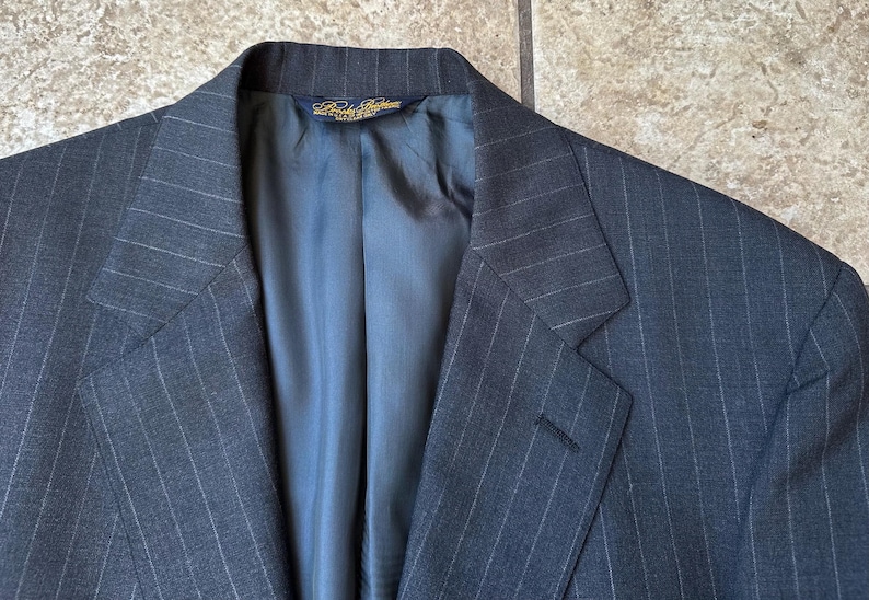 May include: A dark gray pinstripe suit jacket with a blue lining. The jacket has a single button closure and a notch lapel.