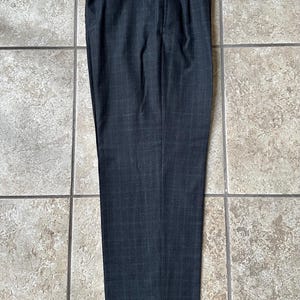 May include: A pair of dark gray dress pants with a subtle plaid pattern. The pants have a single pleat on each side and a button closure at the waist.