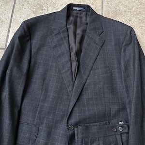May include: A dark gray suit with a subtle plaid pattern. The suit jacket has a single button closure and a notched lapel. The suit pants have a flat front and a belt loop waistband.