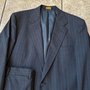 May include: A dark gray pinstripe suit jacket with a single button closure. The jacket has a notch lapel and a welt pocket on the left side.