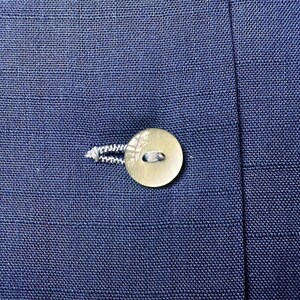 May include: Close-up of a navy blue fabric with a round, off-white button and a buttonhole. The button is attached with white thread. The fabric has a textured appearance.
