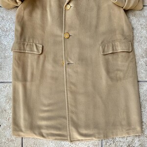 May include: A tan-colored coat with three buttons and two front pockets. The coat is made of a soft, suede-like material. The coat is buttoned up and appears to be in good condition.